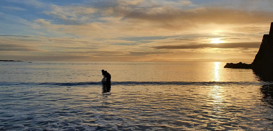 Researcher, Niamh, collects water samples in Galway at sunset