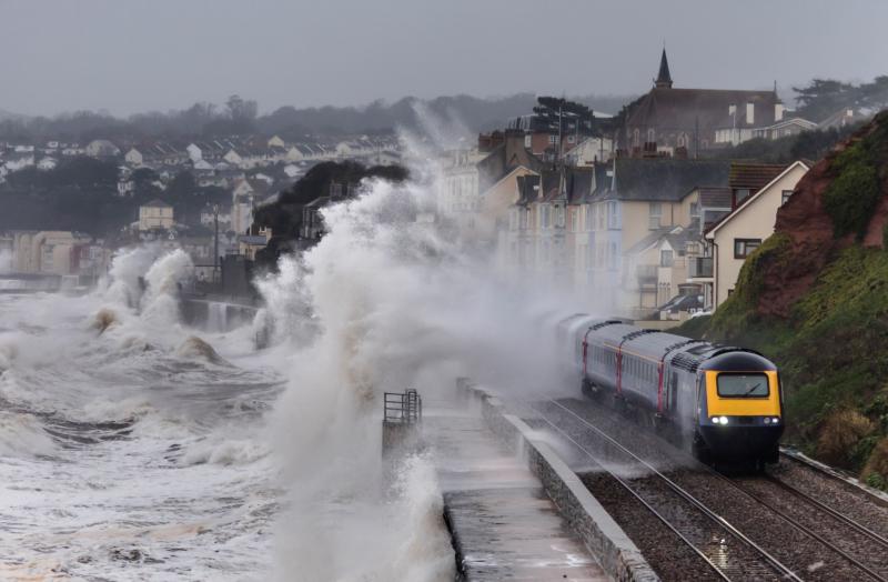 A train passes through crashing waves that are flooding the tracks in Devon, UK.